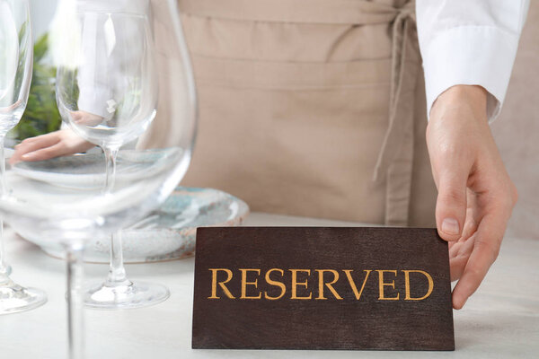 Waiter setting RESERVED sign on restaurant table, closeup