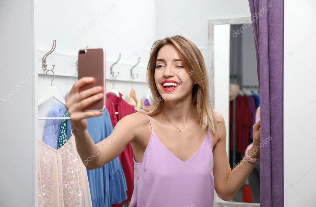 Young woman taking selfie in dressing room. Fashion store