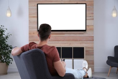 Genç adam evde koltukta TV izliyor. Mockup tasarım için