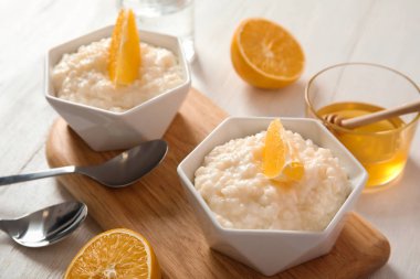 Ahşap masa üzerinde krem sütlaç kaseleri içinde portakal dilimleri ile servis