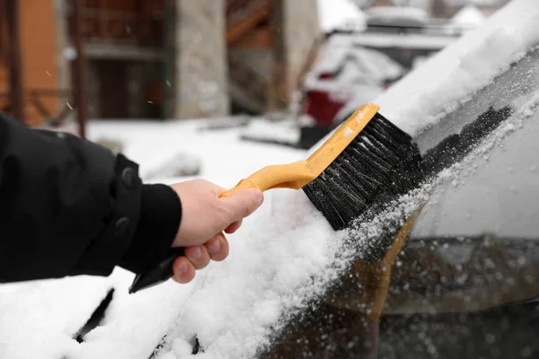 Man cleaning car windshield from snow with brush outdoors, closeup