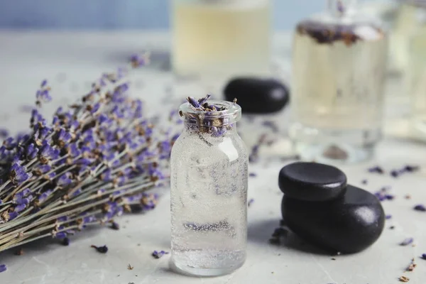 Bottles with natural herbal oil and lavender flowers on color table, closeup