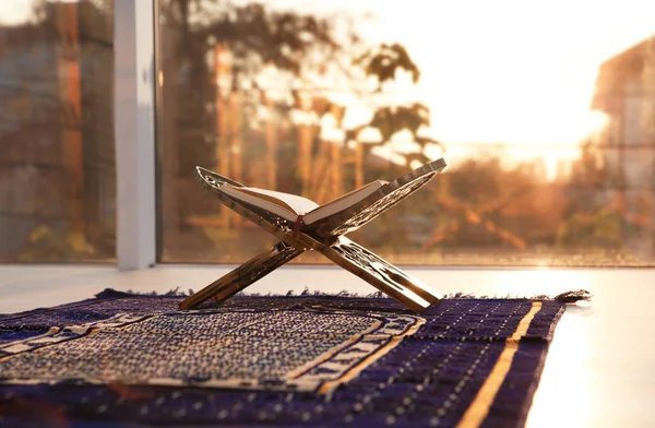 Rehal with open Quran on Muslim prayer rug indoors