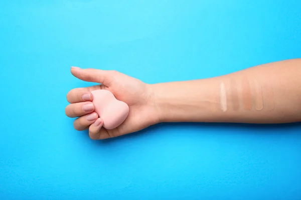 Woman testing different shades of liquid foundation on her hand against color background, closeup