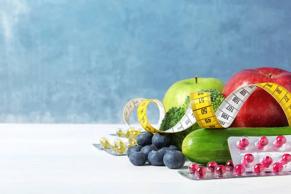 Weight loss pills with measuring tape and healthy food on light table. Space for text