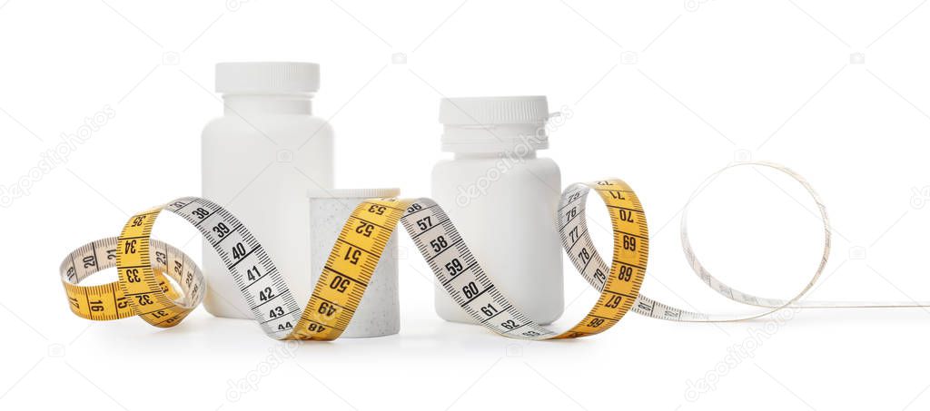 Bottles of weight loss pills and measuring tape isolated on white