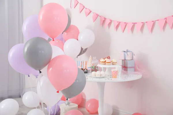 Party treats and items on table in room decorated with balloons