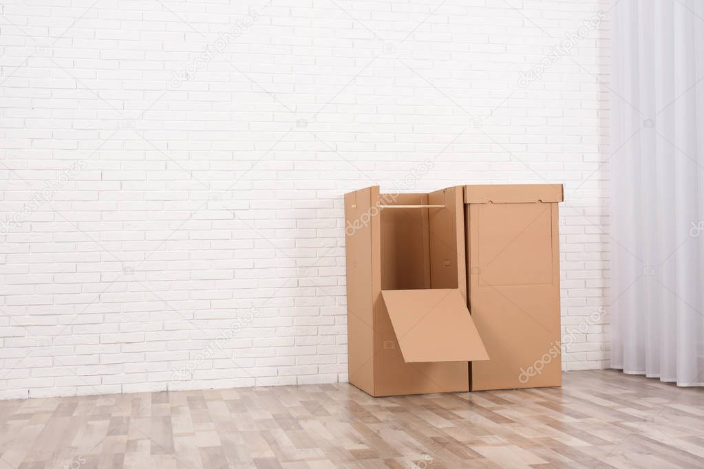 Empty cardboard wardrobe boxes against brick wall indoors. Space for text