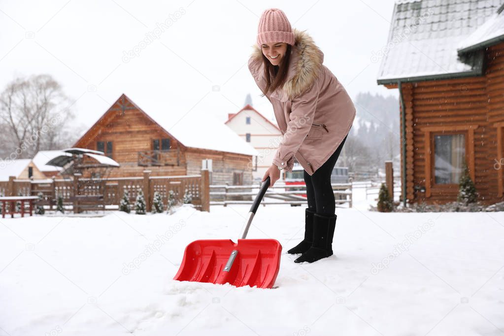 Young woman cleaning snow with shovel near her house