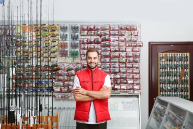 Salesman standing near showcase with fishing equipment in sports shop clipart