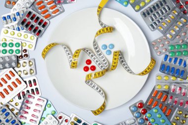 Düz kompozisyon ile kilo kaybı hapları, plaka ve beyaz arka plan üzerinde ölçüm bandı yatıyordu.