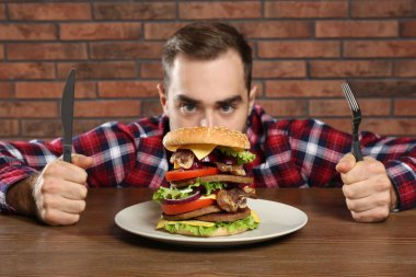 Büyük hamburger masada yemek çatal ile genç aç adam