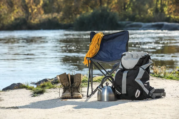 Set of camping equipment on sand near pond
