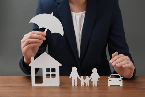 Woman with cutout paper family, house, car and umbrella at table, closeup. Life insurance concept