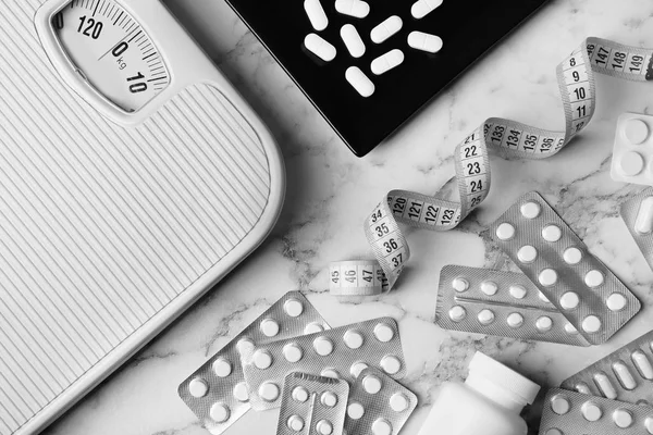 Flat lay composition with weight loss pills, scales and measuring tape on marble background