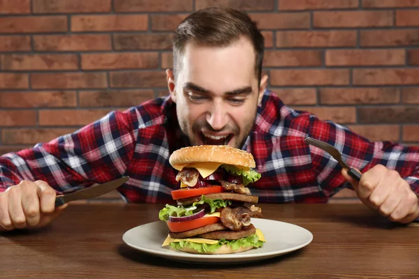 Jovem Faminto Com Talheres Comendo Hambúrguer Enorme Mesa — Fotografia de Stock