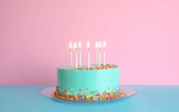 Свежий вкусный праздничный торт со свечами на столе на фоне цвета
