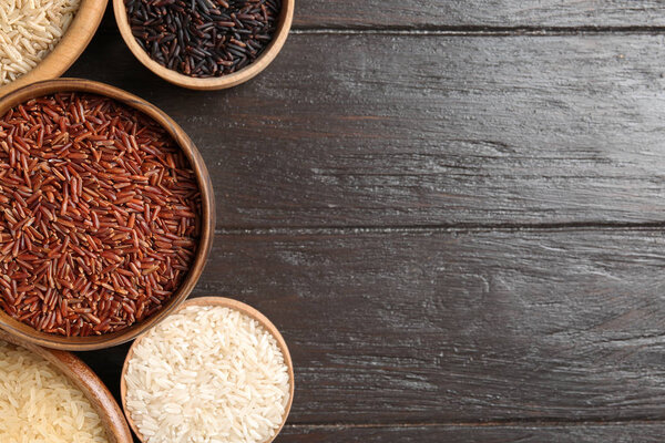 Flat lay composition with brown and other types of rice in bowls on wooden background. Space for text