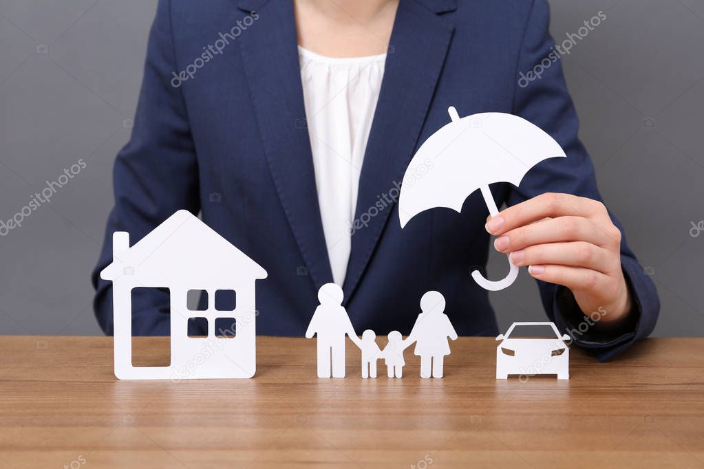 Woman with cutout paper family, house, car and umbrella at table, closeup. Life insurance concept