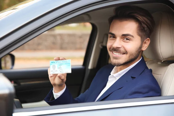 Young man holding driving license in car