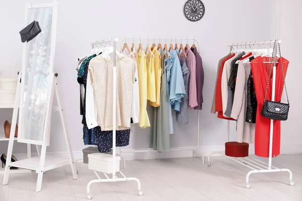 明るい部屋で異なるスタイリッシュな服を着てワードローブ棚 — ストック写真