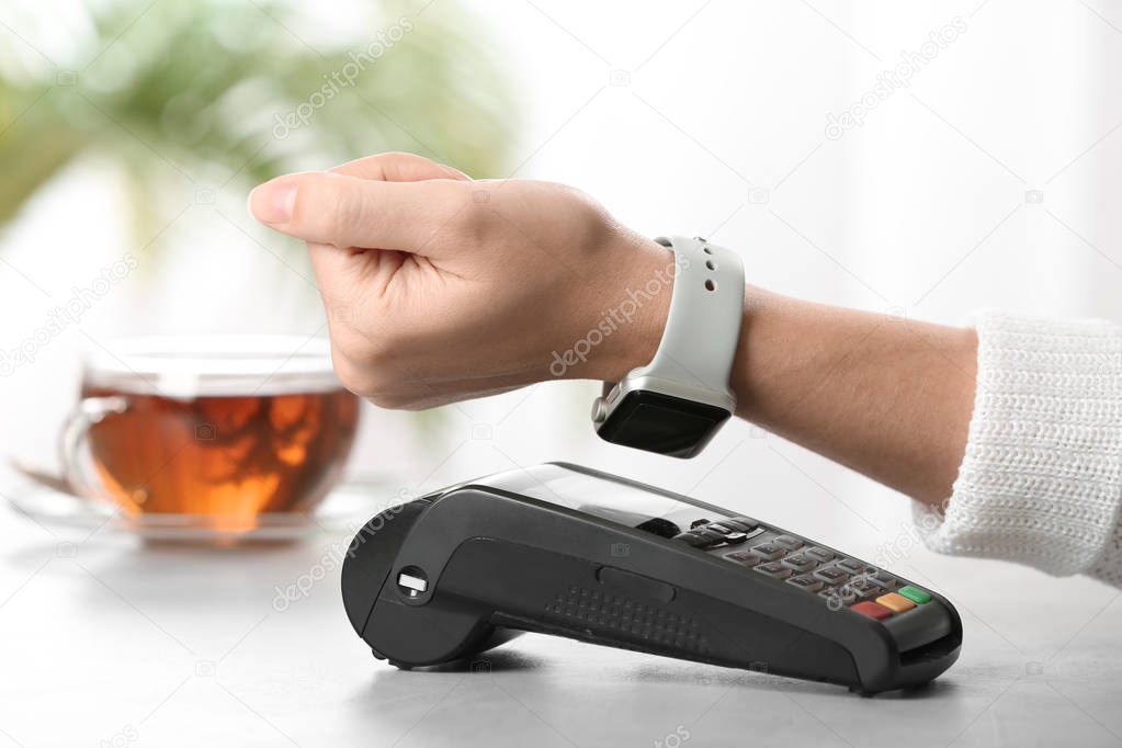 Woman using terminal for contactless payment with smart watch at table, closeup