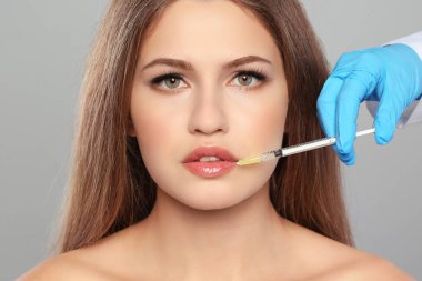 Genç kadın Dudak enjeksiyon gri arka plan üzerine alma. Kozmetik cerrahi