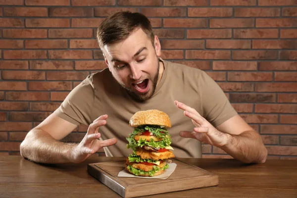 背景色でおいしいハンバーガーを食べる若い男 — ストック写真