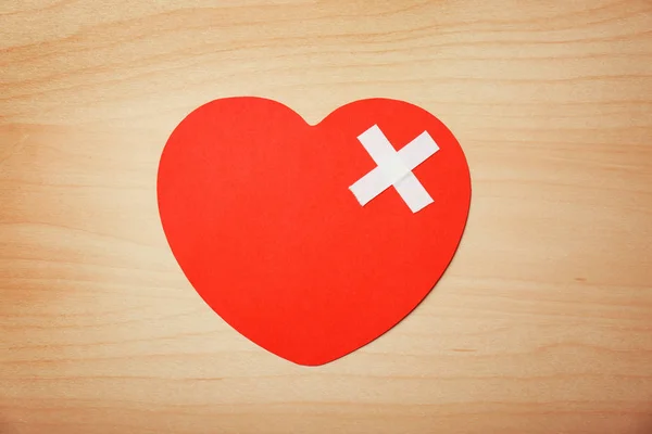 Paper heart with adhesive plasters on wooden background, top view. Relationship problems