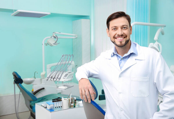 Professional male dentist in white coat at workplace. Space for text