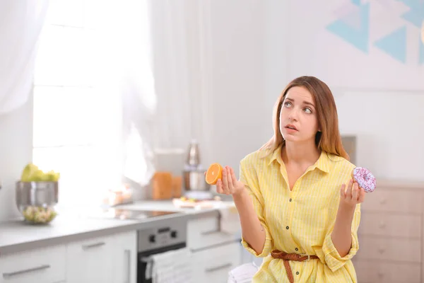 Задумчивая Молодая Женщина Выбирает Между Апельсином Пончиком Кухне Место Текста — стоковое фото