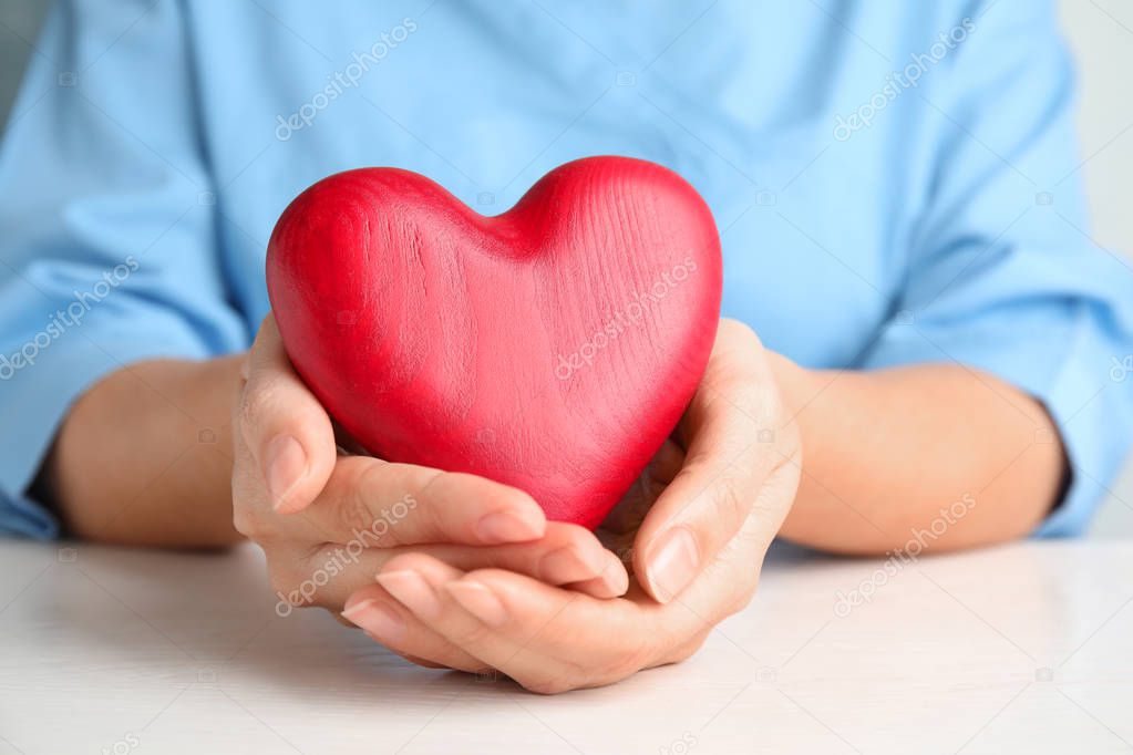 Doctor holding red heart at wooden table, closeup. Cardiology concept