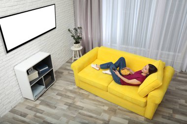 TV izlerken, yemek genç kadın evde kanepede görünümü fişleri. Mockup tasarım için