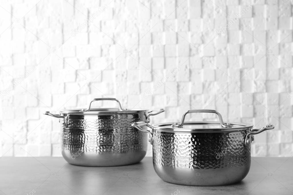 New clean saucepans on table against white wall, space for text