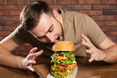 Genç aç adam masada büyük hamburger yeme