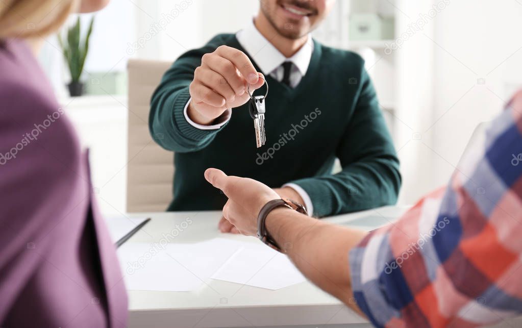 Real estate agent giving keys to young couple in office