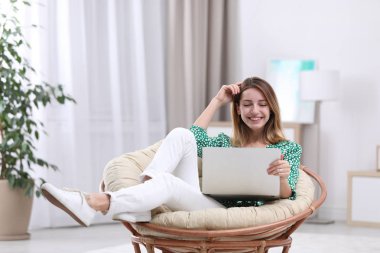 Attractive young woman with laptop in armchair at home clipart