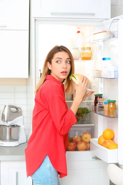 Emotionele Jonge Vrouw Sandwich Eten Buurt Van Open Koelkast Keuken — Stockfoto