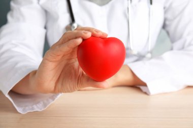 Ahşap masa, tatlı kırmızı kalp tutan doktor. Kardiyoloji kavramı