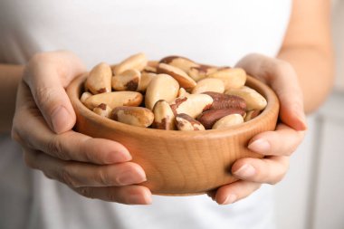 Woman holding bowl with Brazil nuts on blurred background, closeup clipart