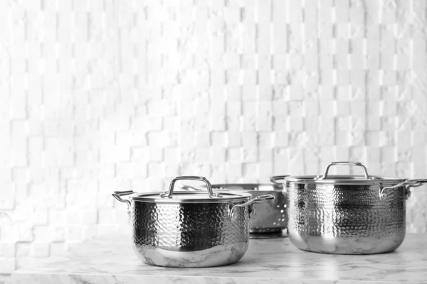 Clean saucepans and colander on table against white wall, space for text