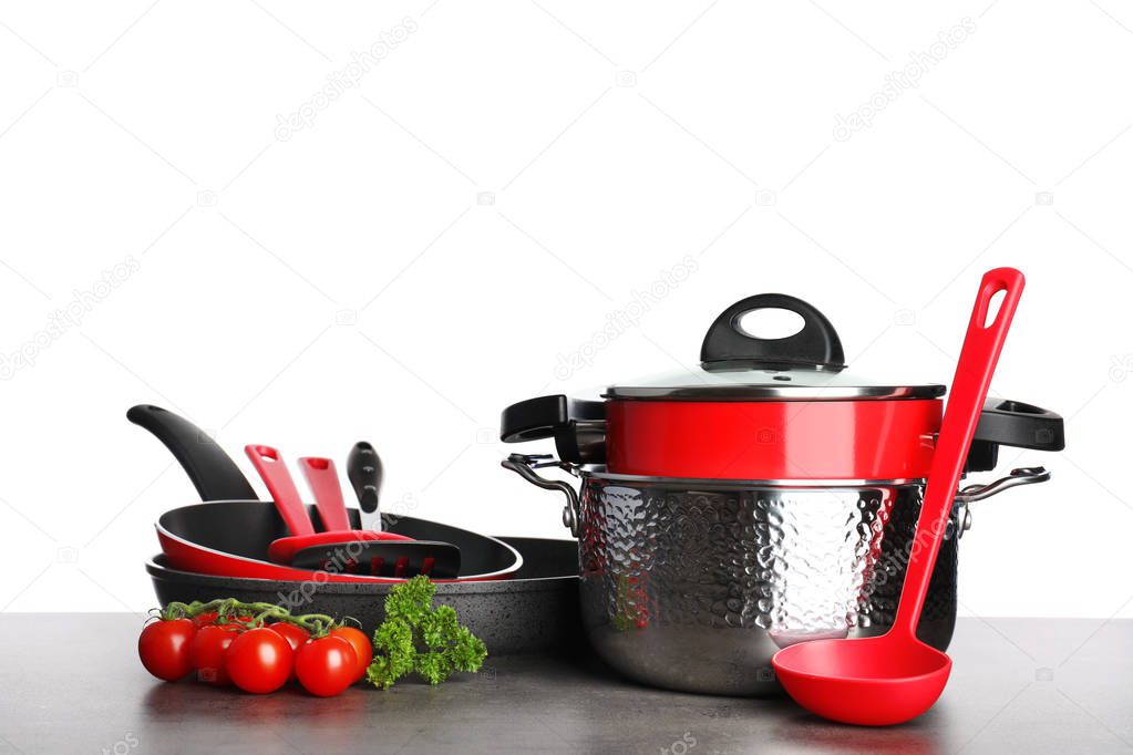 Set of clean cookware, utensils and vegetables on table against white background