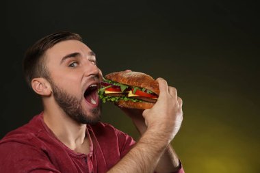 Genç adam renk arka plan üzerinde lezzetli hamburger yeme. Metin için yer