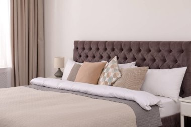 Basit bir odanın içinde, ışık duvarının yanında büyük, rahat bir yatak.