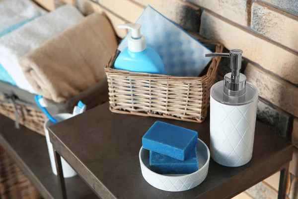 Dish with soap bars and bottle of shampoo on table near brick wall