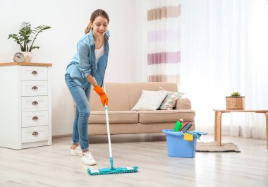 Genç bir kadın oturma odasında yerleri paspasla yıkıyor. Temizlik servisi