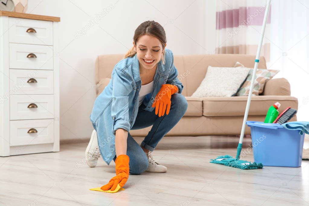 Young woman washing floor with rag and detergent in living room. Cleaning service