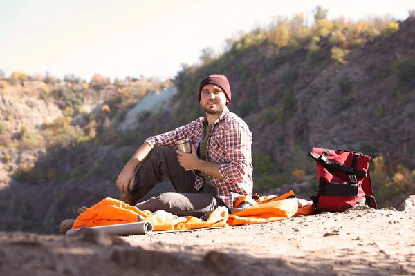 在荒野中 带着热水瓶的雄性露营车坐在睡袋上 — 图库照片