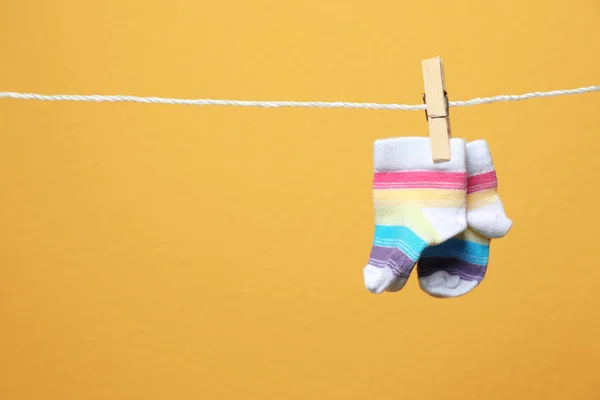 Cute socks for baby on laundry line against color background. Space for text