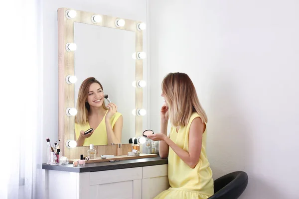 Woman applying makeup near mirror with light bulbs in dressing room